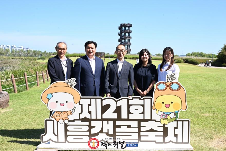 보도자료1-2 20일 하치오지시 대표단이 갯골축제가 열린 갯골 생태공원을 방문해 흔들전망대를 배경으로 기념 촬영을 하고 있다. (사진 왼쪽에서 두 번째가 임병택 시흥시장, 사진 가운데가 나카무라 히토시 하치오지시 부시.jpg
